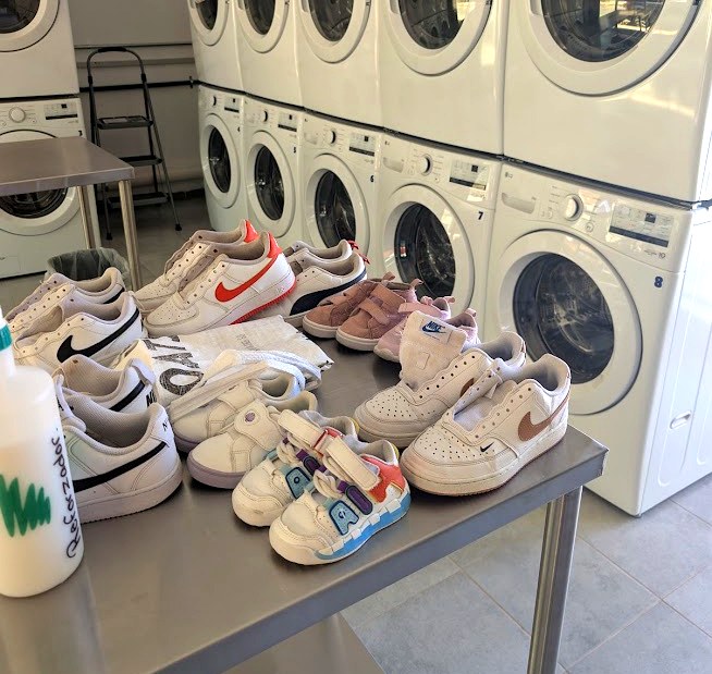 Tenis recién lavados sobre la mesa de trabajo, frente a las lavadoras de Super Clean